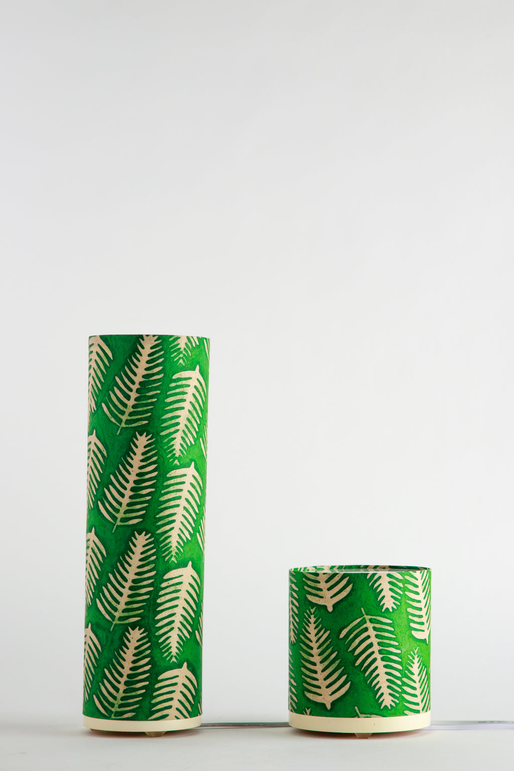 Two green cylindrical paper artistic table lamps made by Branstead Design with leaf pattern on a white background
