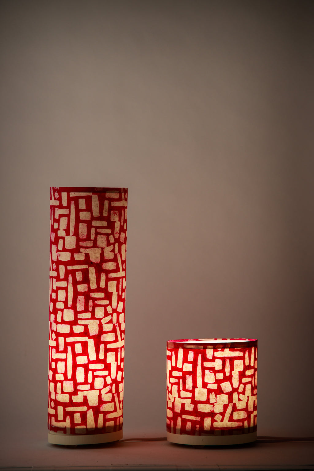 Two cylindrical canvas table lamps made by Branstead Design with geometric red and white pattern on a dark background