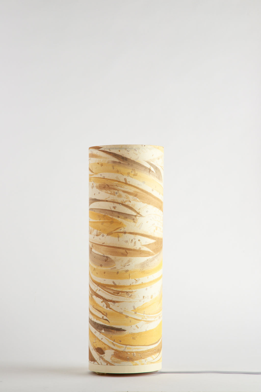 Flux Golden Dune studio table lamp made by Patricia Branstead, unlit on a white background, with layered gold and tan brushstrokes on a cylindrical lamp shade