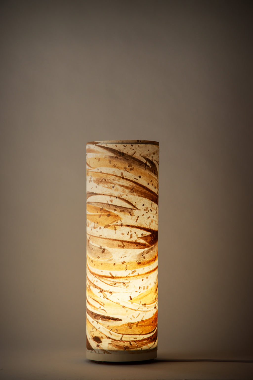 Flux Golden Dune table lamp illuminated in a dim interior, casting a soft golden glow that enhances its earthy tones and painterly texture