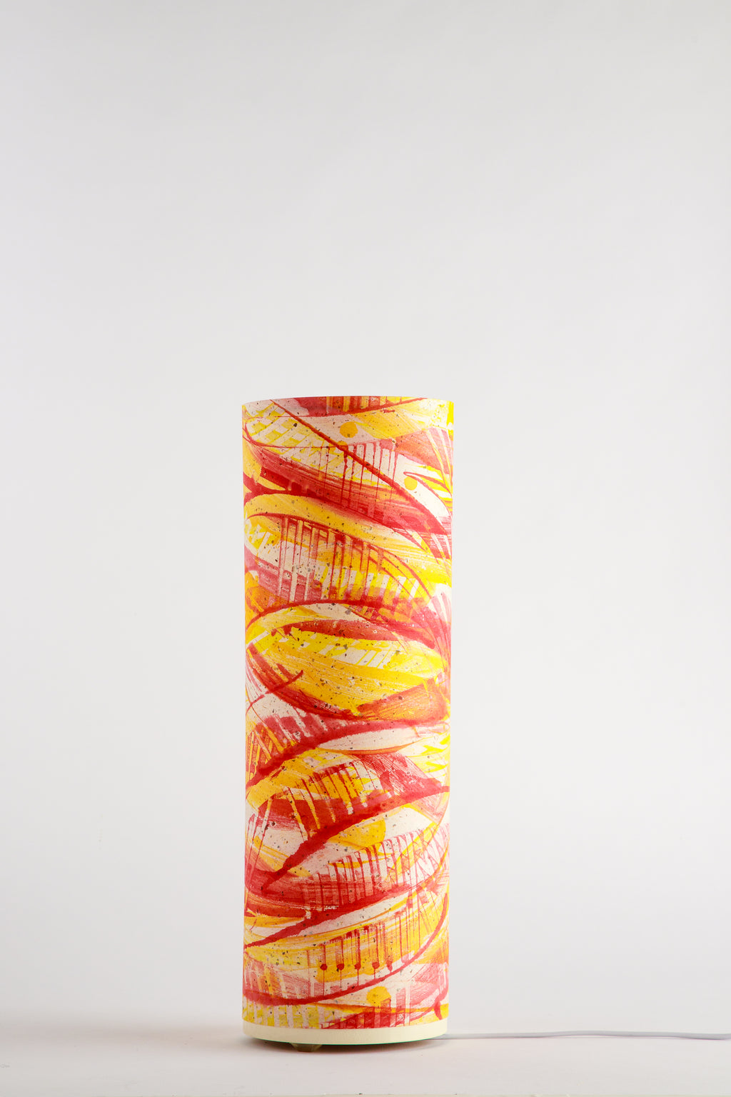 Flux Ember Spiral lamp by Patricia Branstead, unlit on a white background, with bold red and yellow swirling brushstrokes on a cylindrical shade