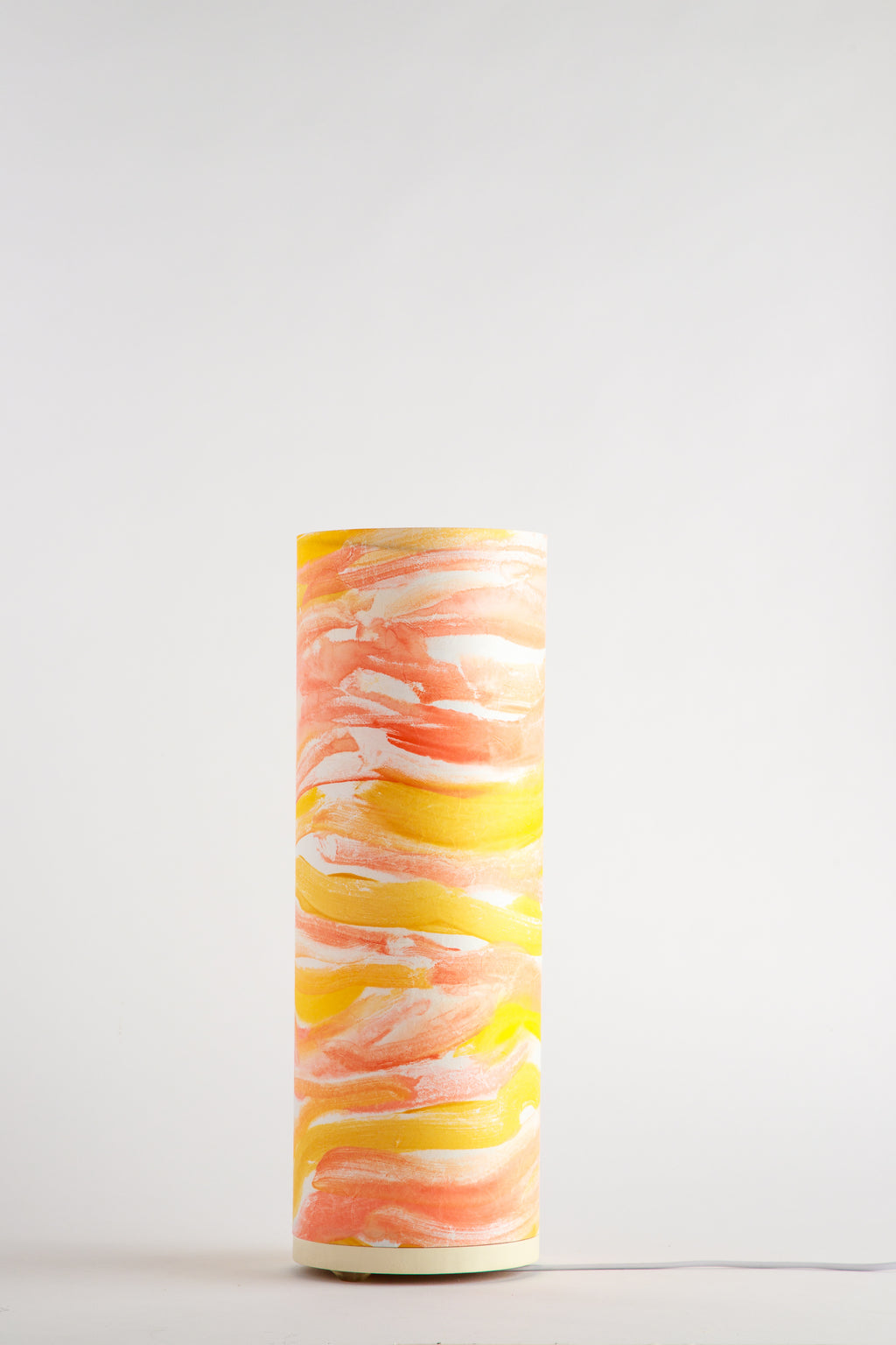 Handcrafted Flux Solar Current table lamp by Patricia Branstead, unlit on a white background, featuring flowing yellow and coral brushstrokes on a cylindrical form