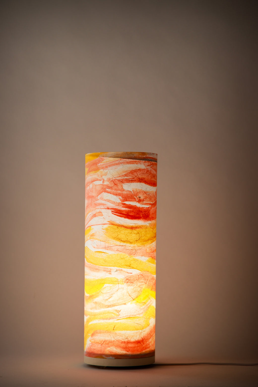 Flux Solar Current bedside cool lamp illuminated in a dim room, casting a warm golden glow that highlights painterly brushstrokes and radiant color transitions