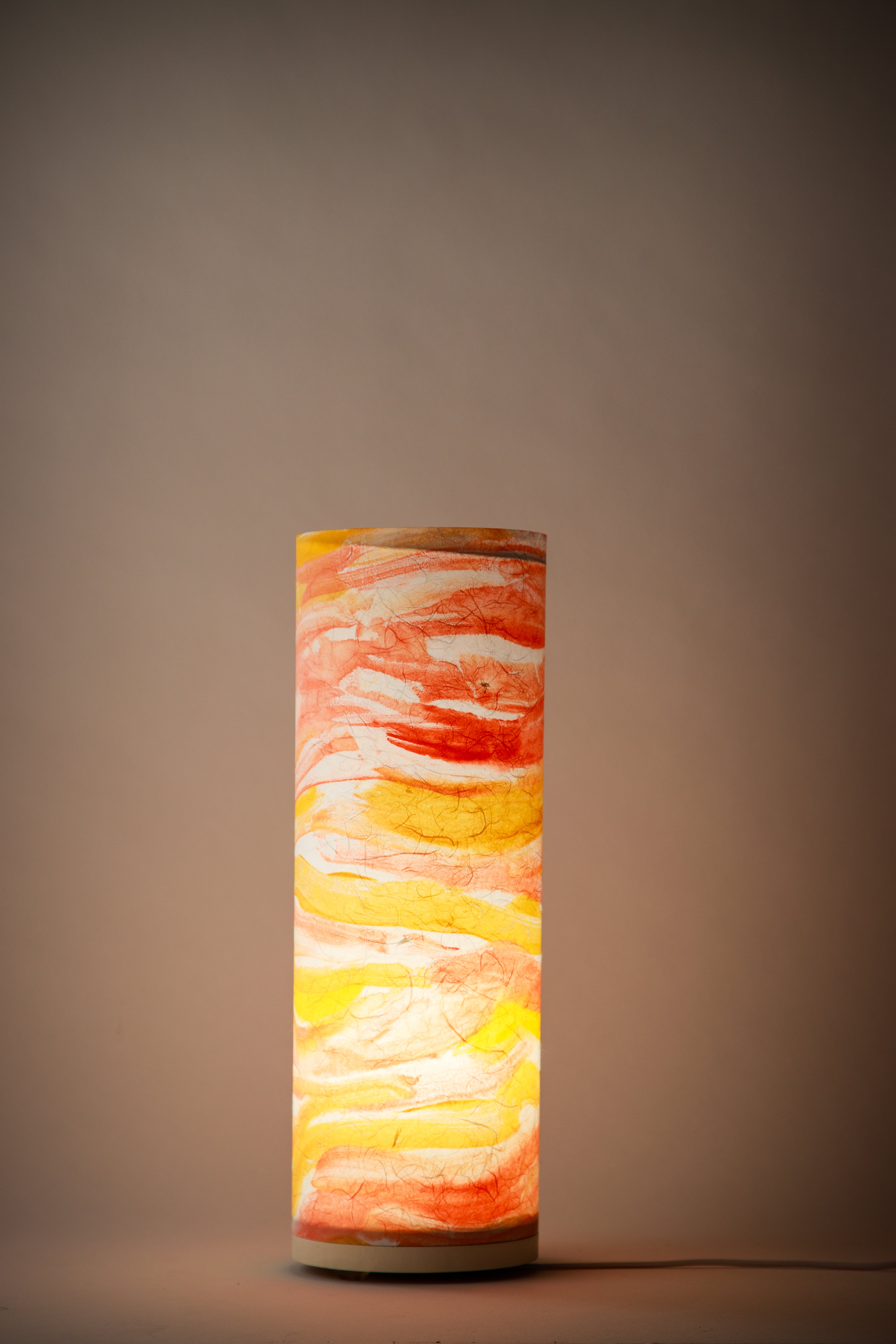 Flux Solar Current bedside cool lamp illuminated in a dim room, casting a warm golden glow that highlights painterly brushstrokes and radiant color transitions