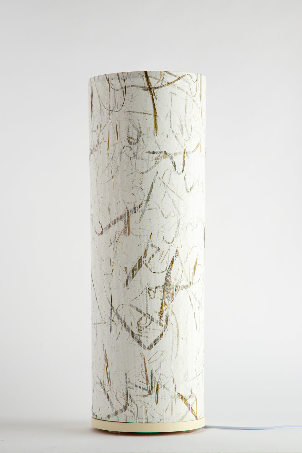 Handcrafted cylindrical table lamp with subtle gold and graphite linework on a soft white background by artist Patricia Branstead