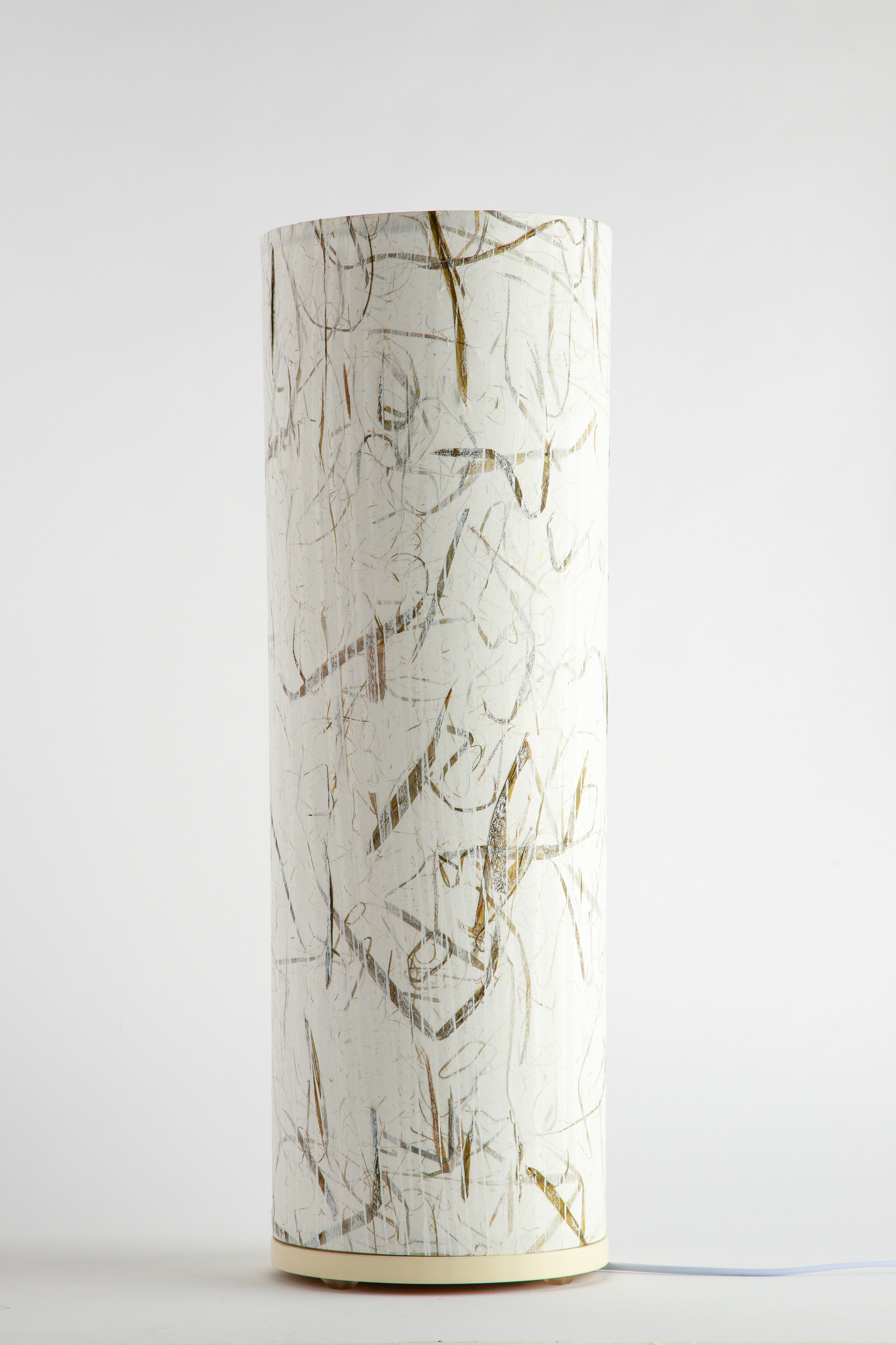 Handcrafted cylindrical table lamp with subtle gold and graphite linework on a soft white background by artist Patricia Branstead