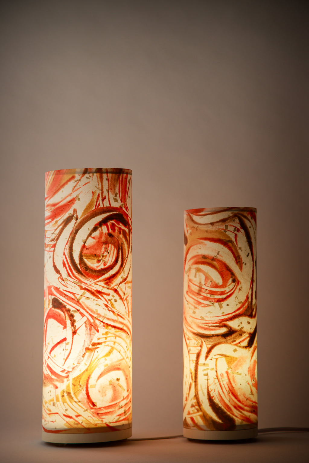 Red and orange abstract bedside lamps glowing in a dark room, showcasing swirling earth-toned brushwork by artist Patricia Branstead.