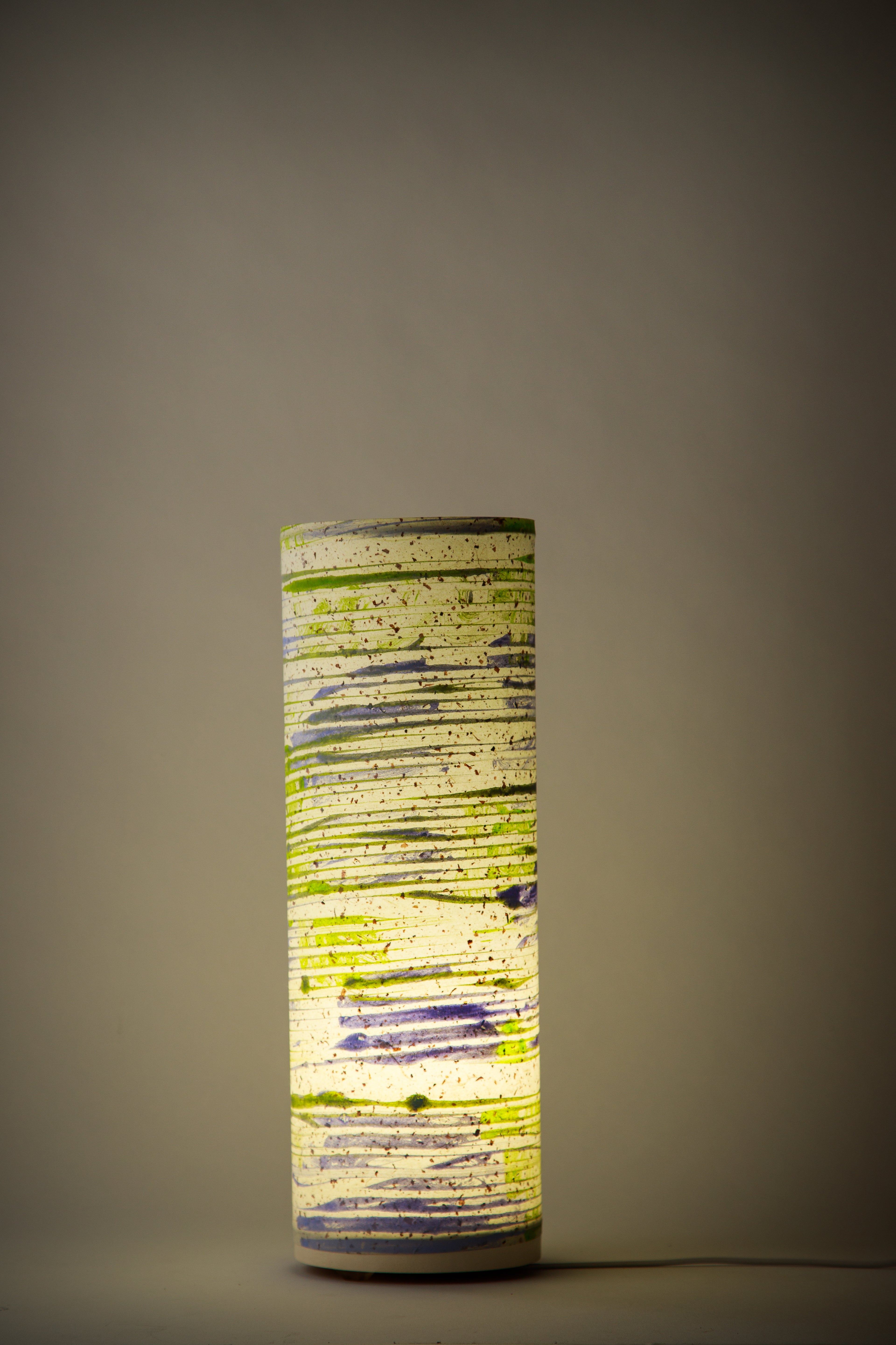 Strata - Chalk & Ash canvas table lamp painted by Patricia Branstead glowing softly, highlighting atmospheric horizontal layers in a dim interior. 